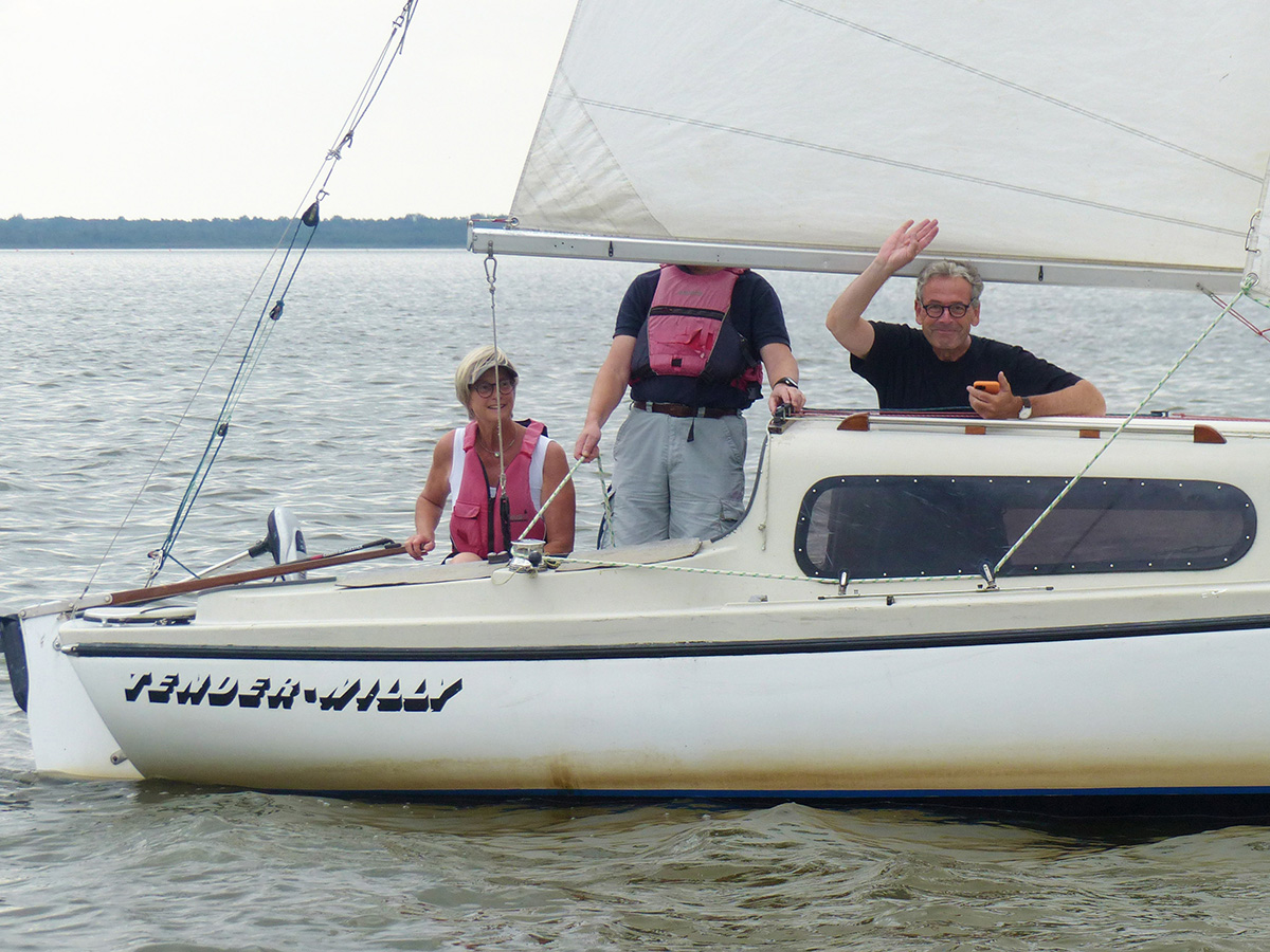 Johannes winkt von seinem Boot mit einem Smartphone in der Hand