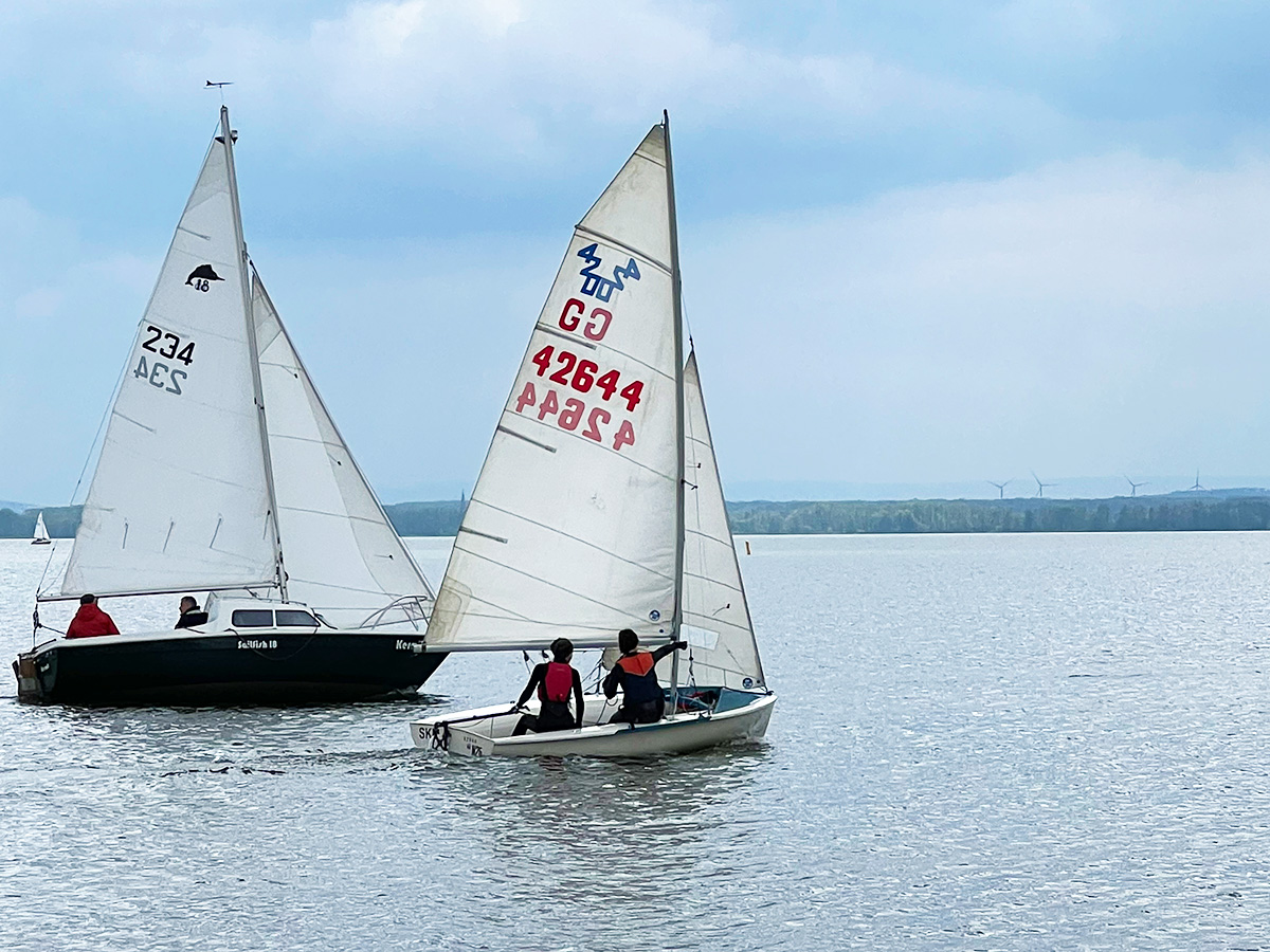 Kielboot und 420er-Jolle segeln über die Startlinie